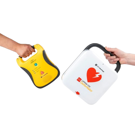 Two hands holding AED defibrillators — a Defibtech and a LIFEPAK CR2 — representing the AED trade-in program